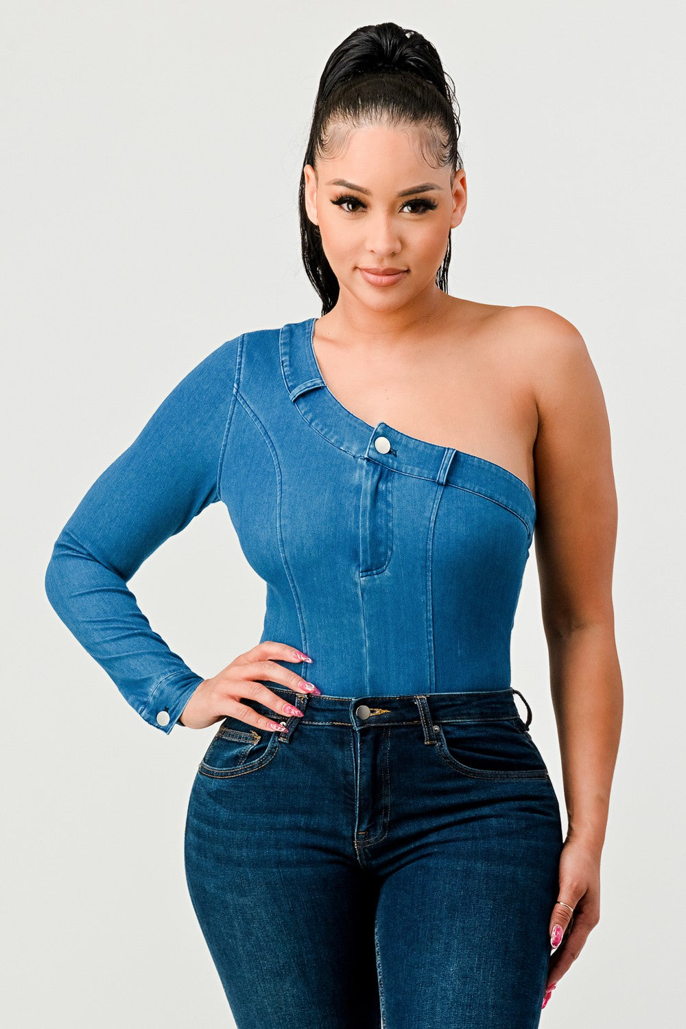 Woman wearing a blue denim one-shoulder top and jeans on a light gray background